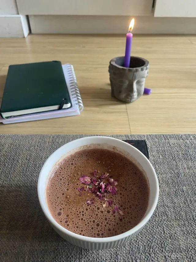 Taza de cacao ceremonial con pétalos junto a un cuaderno y una vela encendida
