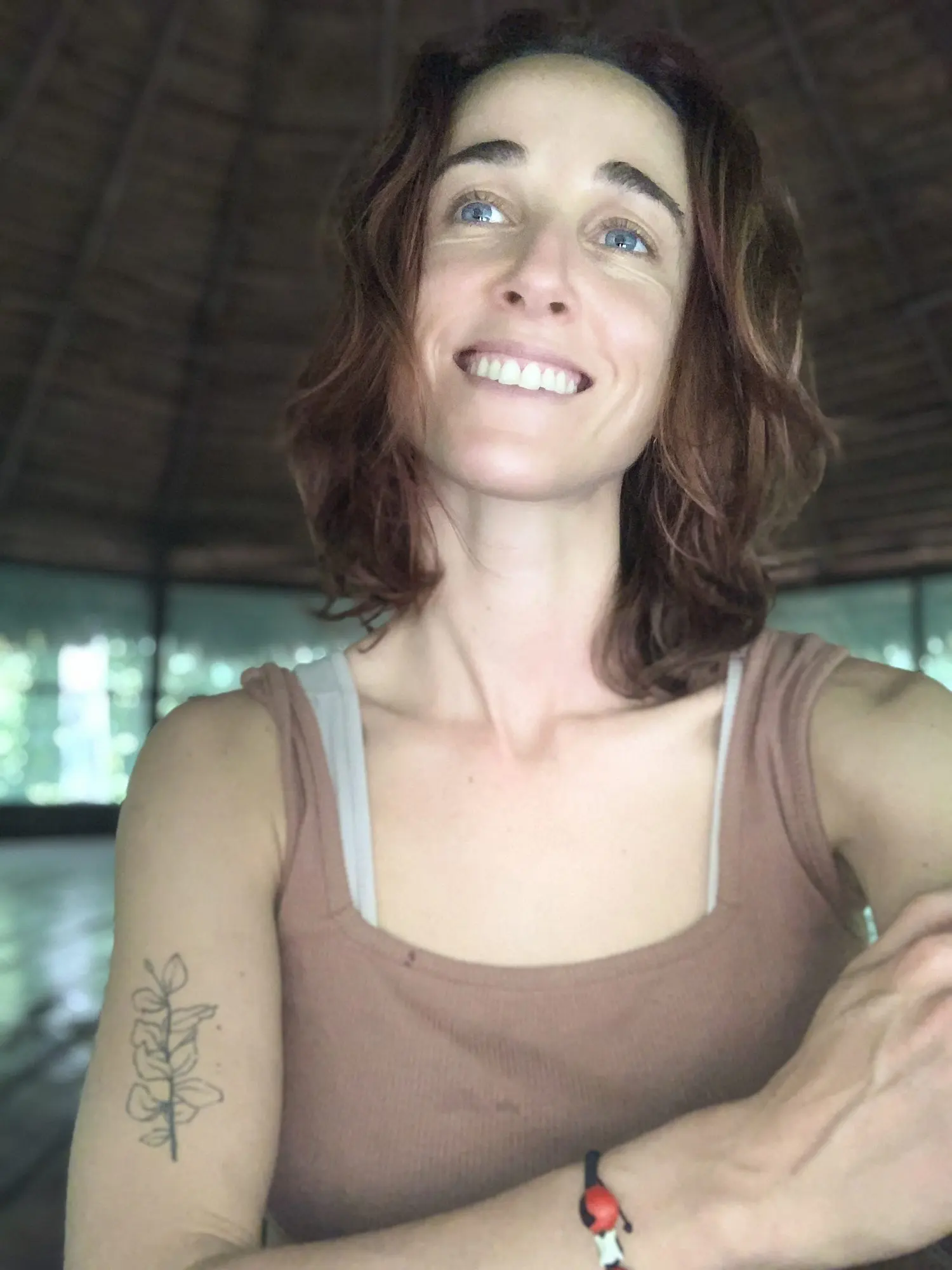 Clari García González sonriendo dentro de una maloca en la selva, con un tatuaje de una rama en el brazo